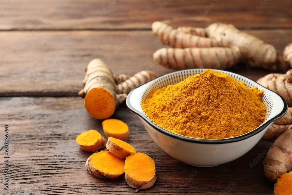 Bowl with aromatic turmeric powder and cut roots on wooden table. Space for text Bowl with aromatic turmeric powder and cut roots on wooden table. Space for text