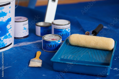 Cans with blue paint, brushes and rollers on house floor
