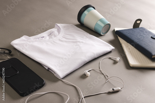 Flat lay of white t shirt, smartphone, earphones and notebooks with copy space on grey background
