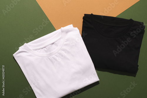 Close up of folded white and black t shirts and copy space on green to orange background