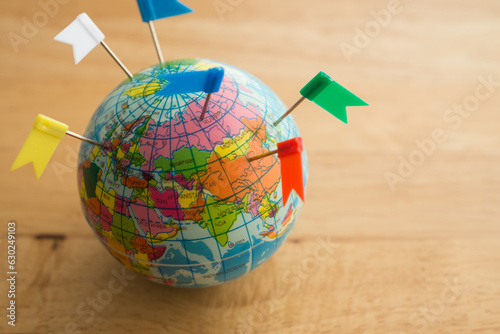 Color flag pins marks on earth globe with wooden table background copy space. Travel holiday vacation destination, business trip, abroad education, company branch concept.