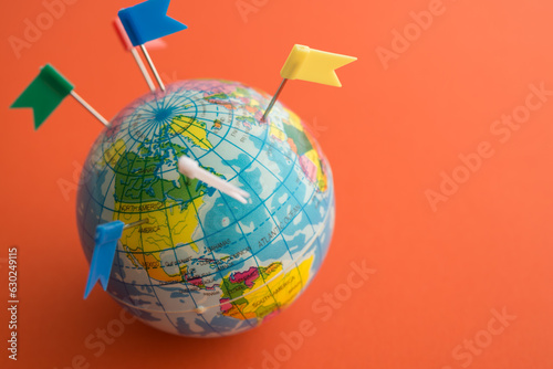 Color flag pins marks on earth globe with orange color background copy space. Travel holiday vacation destination, business trip, abroad education, company branch concept.