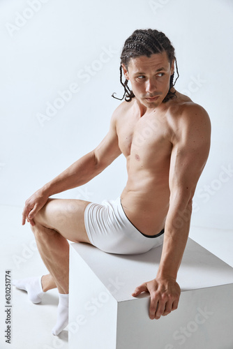 Handsome mature man with braids posing in white underwear against grey background. Male model with muscular, relief body. Concept of men's beauty, body care, sport, wellness, healthy lifestyle, ad photo