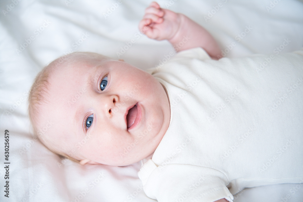 healthy smiling baby lies on his back on bed on white bedding. top view healthy smiling baby lies on his back on bed on white bedding. top view