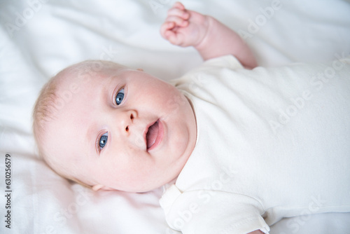 healthy smiling baby lies on his back on bed on white bedding. top view