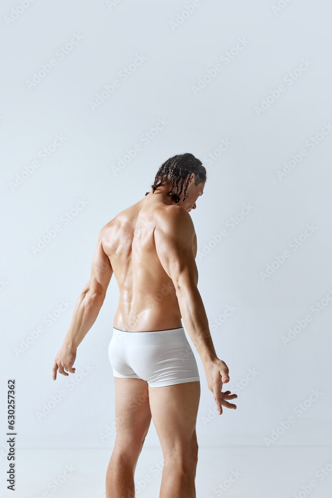Rear view image of man with muscular body posing shirtless in underwear against grey studio background. Relief back, healthy body. Concept of men's beauty, body, sport, wellness, healthy lifestyle, ad Rear view image of man with muscular body posing shirtless in underwear against grey studio background. Relief back, healthy body. Concept of men's beauty, body, sport, wellness, healthy lifestyle, ad