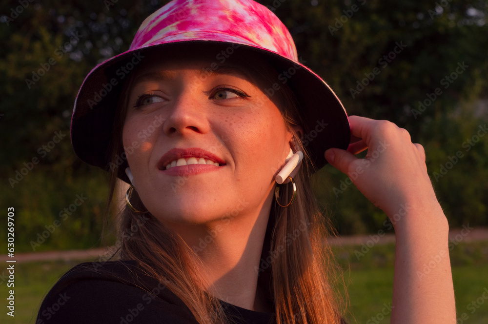 beautiful young girl with freckles in a bright hat listens to music in white air poods