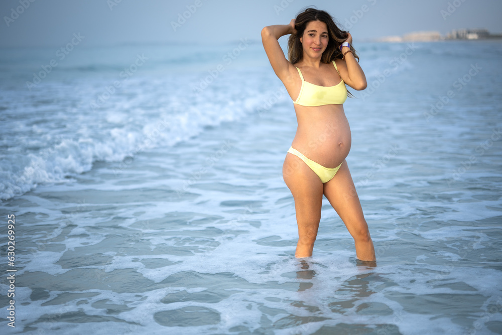 Beautiful pregnant woman in a bikini posing on the beach.