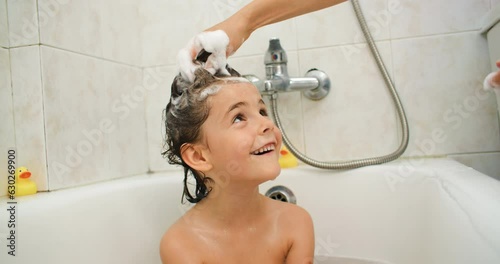 Mom soaps her daughter's hair with shampoo and washes off in the shower. The child takes a bath and bathes. High quality 4k footage