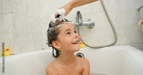 Mom soaps her daughter's hair with shampoo and washes off in the shower. The child takes a bath and bathes. High quality 4k footage photo