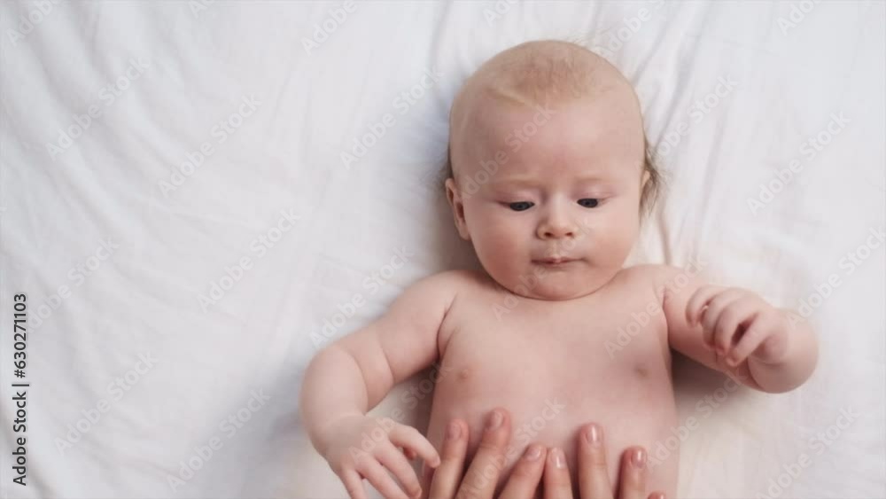 Top view of mother hands doing massage tummy of cute newborn. Nice caucasian infant baby lying on cozy bed at back. Adorable baby boy with smiling face, relaxing time doing belly massage mom at home Top view of mother hands doing massage tummy of cute newborn. Nice caucasian infant baby lying on cozy bed at back. Adorable baby boy with smiling face, relaxing time doing belly massage mom at home