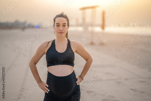 Portrait of beautiful pregnant woman standing on the beach at sunset. Working out, yoga and pregnancy concept.