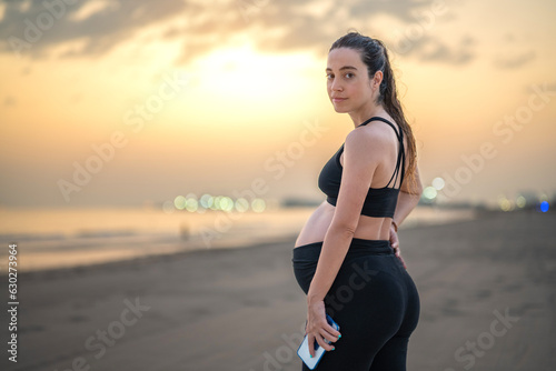 Portrait of nine months pregnant woman holding phone against sunset sky on the beautiful summer beach.
