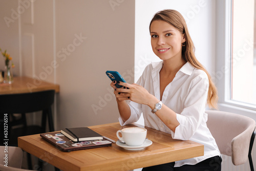 Businesswoman using phone during break in cafe. Female have rest and drink coffee