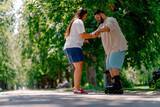 Young couple girl holds hands of the guy who is roller skating and helps him to learn to skate in the park plus size models