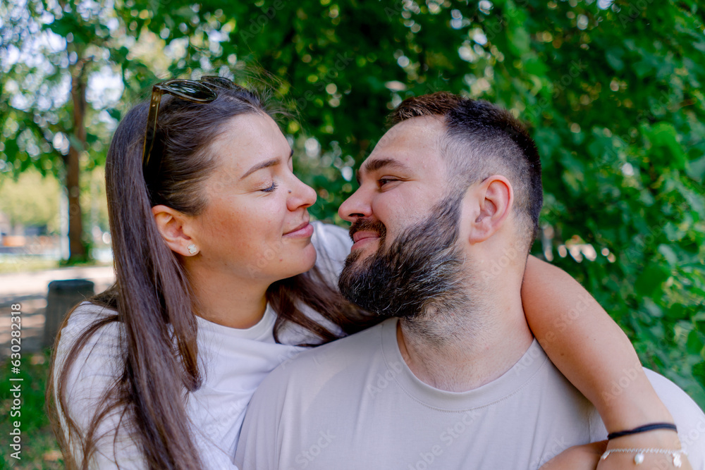 Fototapeta premium Portrait of a young couple of a man and a woman standing in an embrace and kissing during a date on the background of a park plus size model