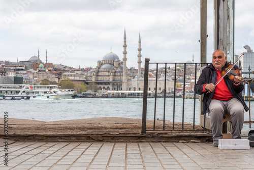 Istanbul, Turkey - 23 April 2023: View of a person playing the violin on the street along the Bosphorus channel with Suleymaniye Mosque in background in Istanbul, Turkey.