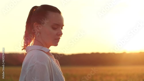 Woman watching the sunset on field. Cinematic shot of young female enjoying nature landscape on summer evening