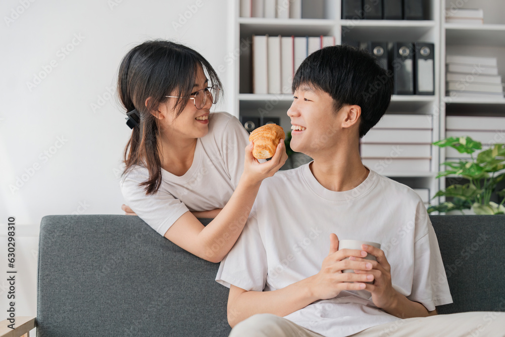 Young couples spend holidays in the living room. The young man was wearing comfortable clothes, showing his face, satisfied with the taste of snacks. Eating croissant on the sofa Young couples spend holidays in the living room. The young man was wearing comfortable clothes, showing his face, satisfied with the taste of snacks. Eating croissant on the sofa