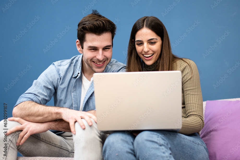 happy young couple sit on couch and using laptop. Cheerful couple smiling and searching on computer