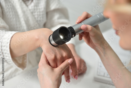 Beautician examine the skin on the female hand with a dermatoscope