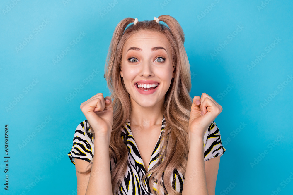 Photo of impressed cheerful girl ponytails hairdo dressed striped blouse clenching fists win lottery isolated on blue color background Photo of impressed cheerful girl ponytails hairdo dressed striped blouse clenching fists win lottery isolated on blue color background
