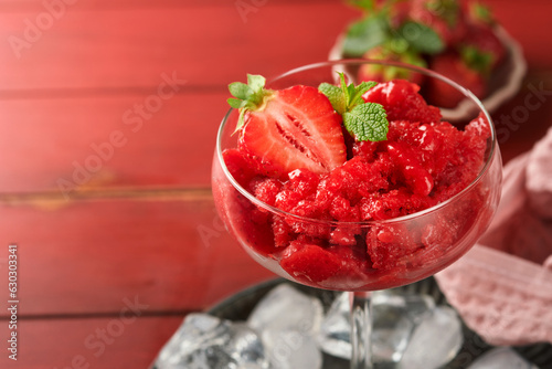 Strawberry granita or fresh berry sorbet in glass on old red wooden table background. Texture of ice cream or sorbet. Ice cream with strawberry and mint. Sorbet recipe. Summer treat. Selective focus. photo
