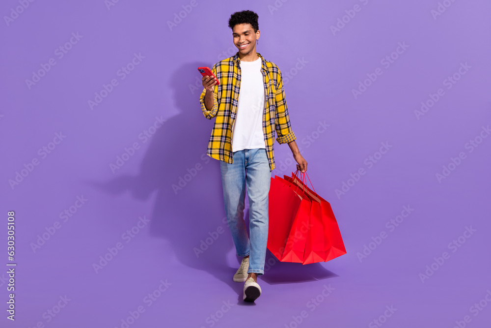 Full size photo of cheerful person hold bags use smart phone walking isolated on violet color background