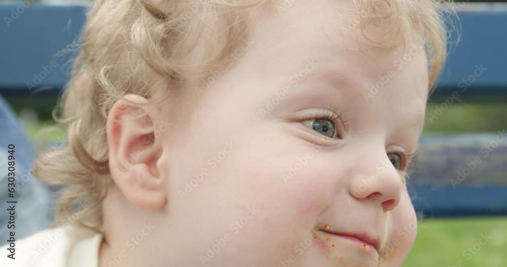 Toddler boy enjoys eating pastries sitting on blue bench with mother in city park. Son eating bun calls friend and wants to play in park Toddler boy enjoys eating pastries sitting on blue bench with mother in city park. Son eating bun calls friend and wants to play in park