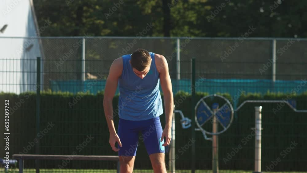 Caucasian young athletic build sprint racer in blue sportswear assuming a starting position in the starting block, beyond starting line, front view. Caucasian young athletic build sprint racer in blue sportswear assuming a starting position in the starting block, beyond starting line, front view.