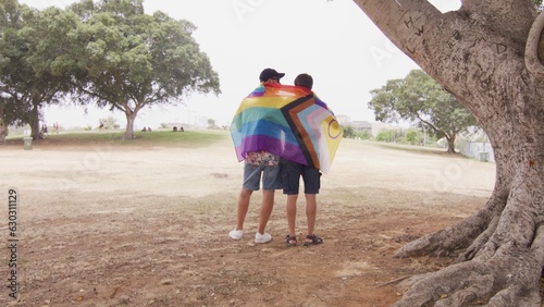 Back shot of two young men hugging with LGBT flag 