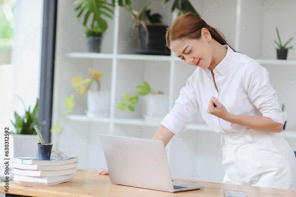 Asian businesswoman is smiling with happiness and success gesture to get good news. Working in front of laptop in the office. Asian businesswoman is smiling with happiness and success gesture to get good news. Working in front of laptop in the office.