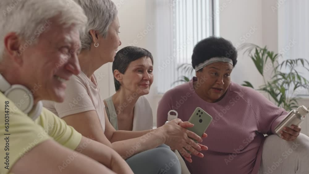 Rack focus shot of cheerful senior women and man having discussion, laughing and smiling while resting after group fitness workout Rack focus shot of cheerful senior women and man having discussion, laughing and smiling while resting after group fitness workout