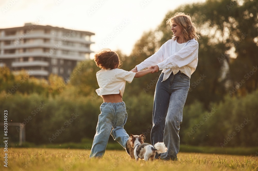 Obraz premium Beautiful mother with her little daughter and dog are on the summer field together