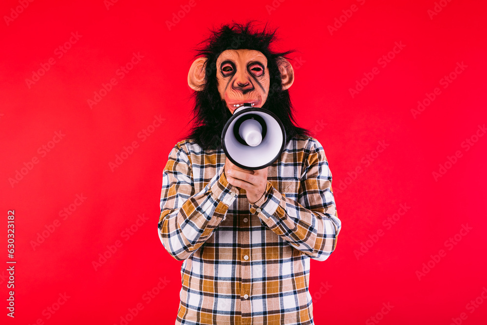 Fototapeta premium Man with chimpanzee monkey mask and plaid shirt, shouting with a megaphone, on red background.