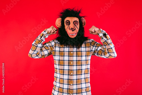 Photography Man with chimpanzee monkey mask and checkered shirt clenching his arms and fists as a sign of strength, on red background