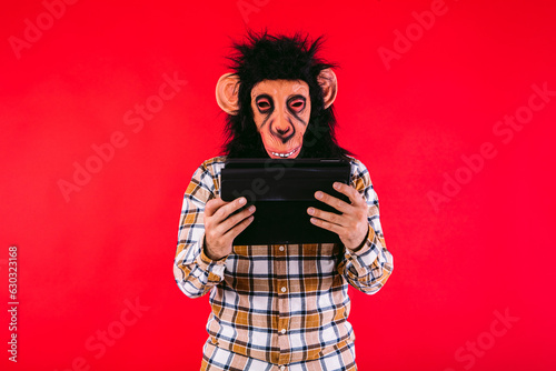 Canvas Print Man with chimpanzee monkey mask and checkered shirt, using a tablet, on red background