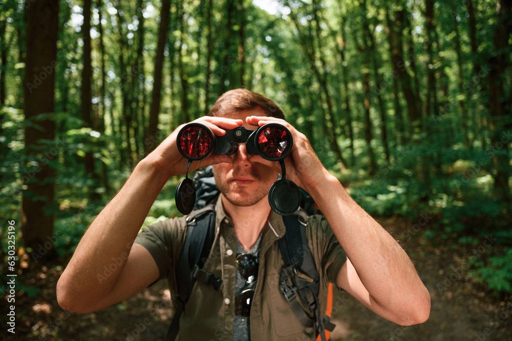 Looking through the binoculars. Tourist in summer forest. Conception of exploration and leisure Looking through the binoculars. Tourist in summer forest. Conception of exploration and leisure
