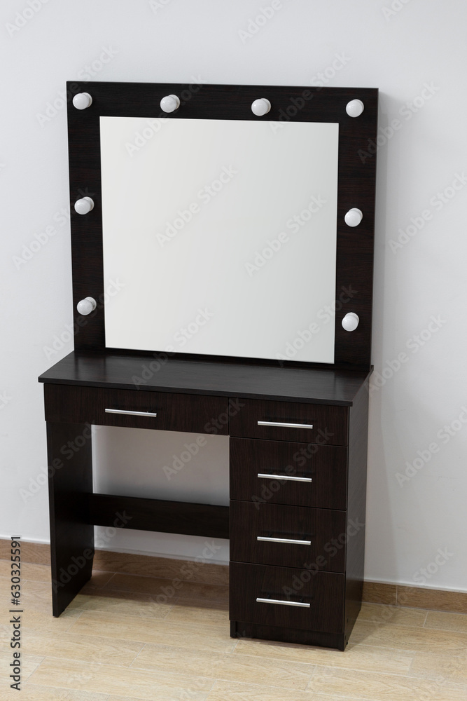 Modern dark makeup dressing table with mirror and backlight against a white wall. Modern dark makeup dressing table with mirror and backlight against a white wall.