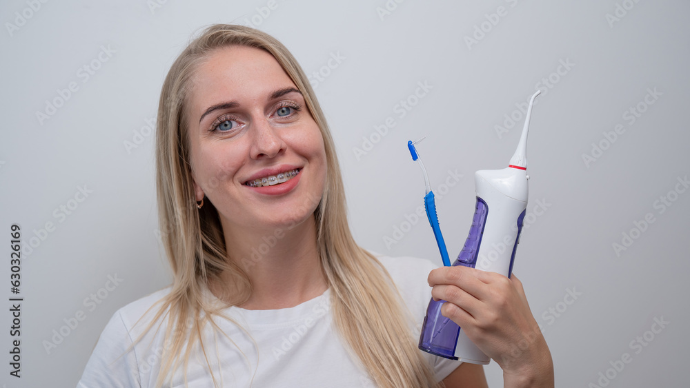 Smiling caucasian woman with braces on her teeth holding an irrigator and a toothbrush. Smiling caucasian woman with braces on her teeth holding an irrigator and a toothbrush.
