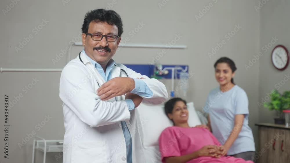 Rack focus shot, confident indian doctor standing with crossed arms in front of patient by looking camera at hospital - concept of professional occupation, expertise and successful treatment Rack focus shot, confident indian doctor standing with crossed arms in front of patient by looking camera at hospital - concept of professional occupation, expertise and successful treatment