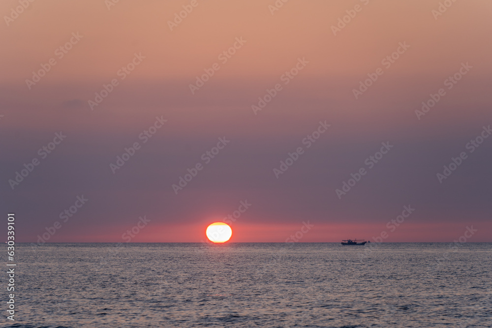 바다 너머로 지는 태양과 바다위에 떠있는 고기잡이 배