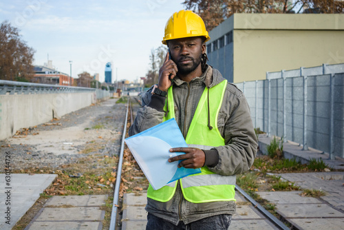 portrait of black man maintenance worker talking on the phone standing on the railway tracks. © SETO fotografias