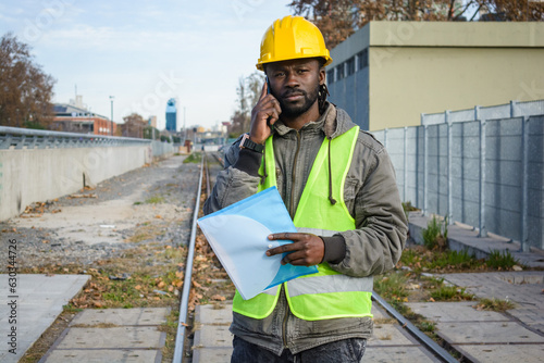 portrait of black man maintenance worker talking on the phone standing on the railway tracks.