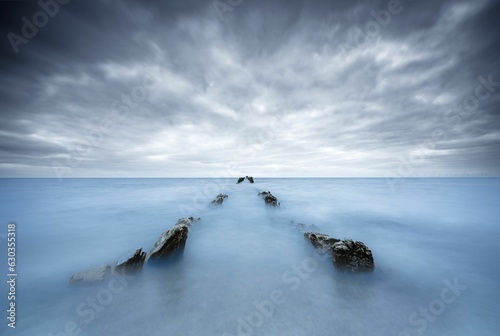 rocks in the ocean with clouds above them on an overcast day