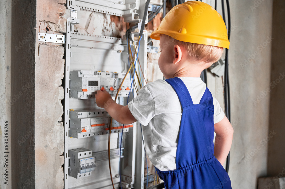 Side view of child fixing electrical switchboard or distribution board in apartment under renovation. Boy electrician repairing household electrical panel with automatic fuses. Side view of child fixing electrical switchboard or distribution board in apartment under renovation. Boy electrician repairing household electrical panel with automatic fuses.