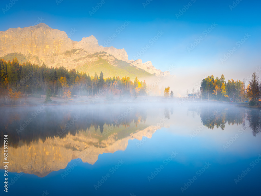 Fall. A foggy morning during dawn. Autumn trees on the river bank. Mountains and forest. Reflections on the surface of the lake. Banff National Park, Alberta, Canada.