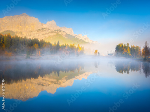 Fall. A foggy morning during dawn. Autumn trees on the river bank. Mountains and forest. Reflections on the surface of the lake. Banff National Park, Alberta, Canada.