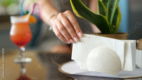 Woman takes paper napkin from ceramic napkin holder on served table. Napkin holder in cafe photo