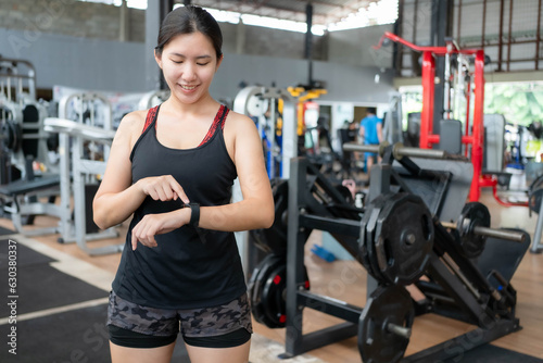 Asian woman looking at smartwatch to check heart rate during exercise at gym
